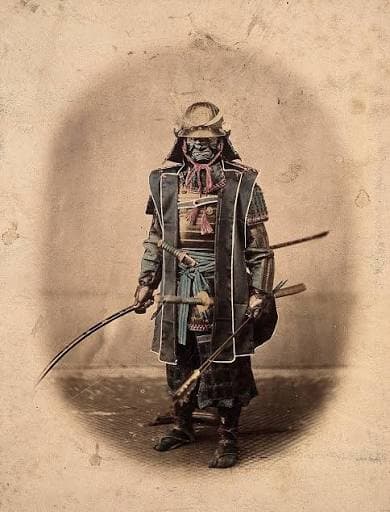 A samurai standing in full armour, holding a drawn sword.